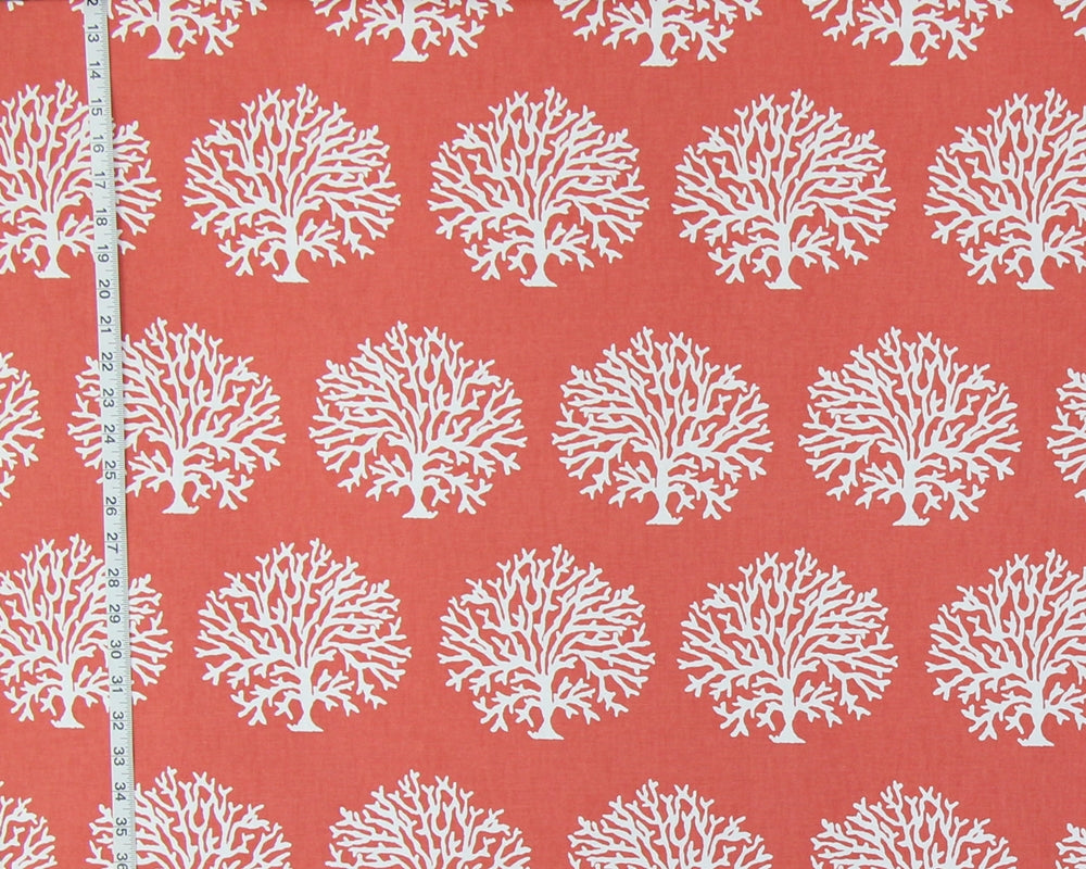 Coral red fabric with a repeating white coral tree pattern, shown with a white measuring tape along the left edge for scale.