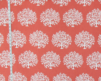 Coral red fabric with a repeating white coral tree pattern, shown with a white measuring tape along the left edge for scale.