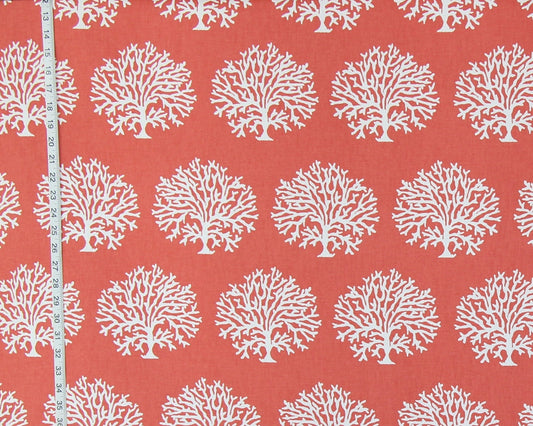 Coral red fabric with a repeating white coral tree pattern, shown with a white measuring tape along the left edge for scale.