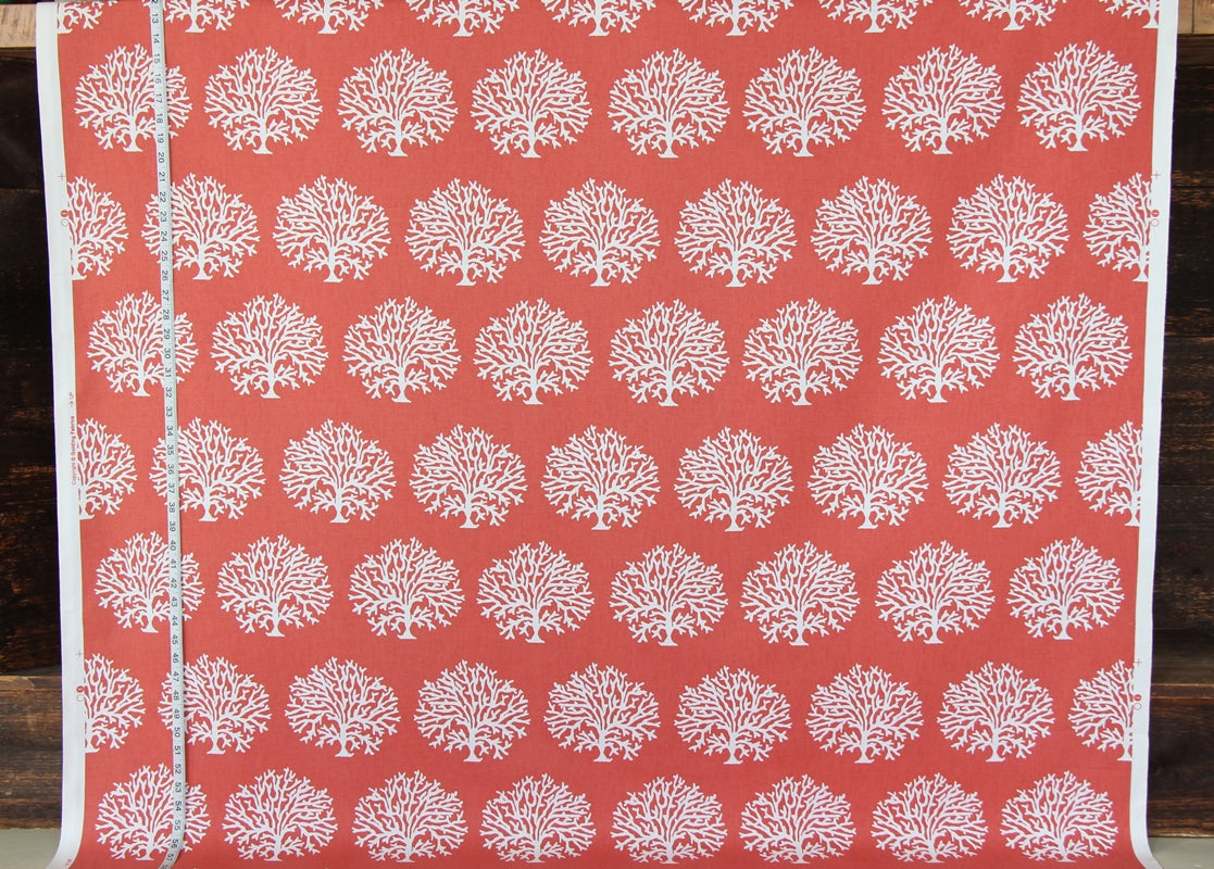 A close-up of a coral red fabric or wallpaper featuring a repeating white tree-of-life pattern, with a white border and a silver seam line visible on the left.