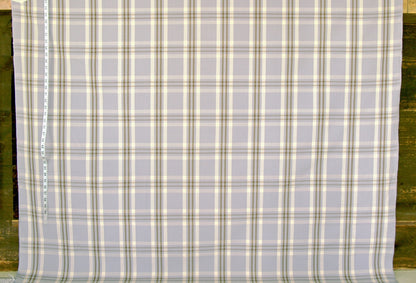 A close-up of a plaid fabric with a light gray base and intersecting cream, olive green, and tan stripes, shown flat with a measuring tape visible along the left edge.