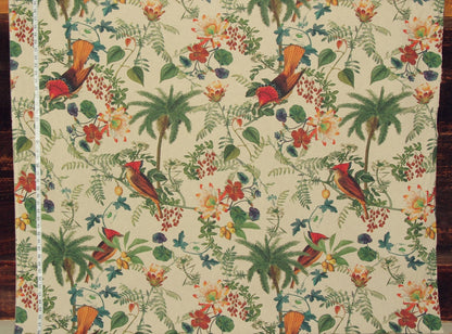 A close-up of a tropical fabric featuring a repeating pattern of red and orange birds, green palm trees, and orange flowers on a cream background, with a white measuring tape visible along the left edge.