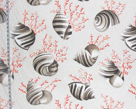 A close-up of a fabric or wallpaper pattern featuring realistic striped seashells and coral branches in coral red and gray on a warm off-white background. A measuring tape is visible along the left edge to indicate scale.