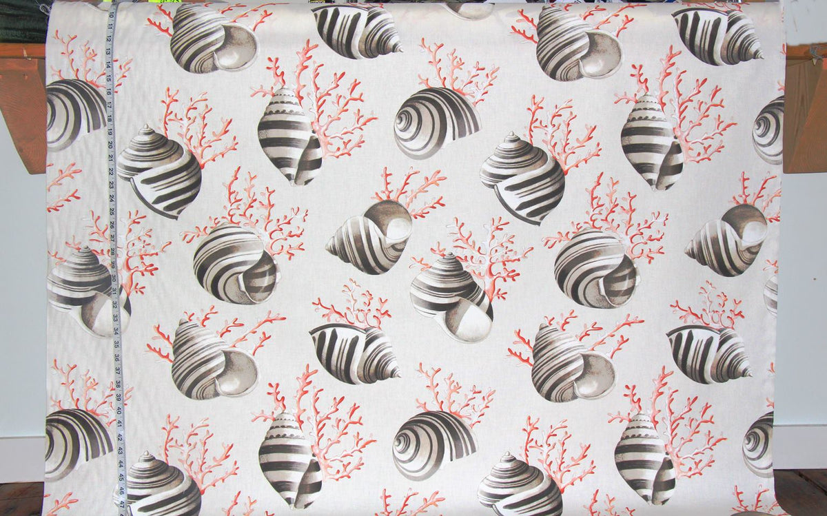 A white fabric panel featuring a repeating pattern of striped seashells and coral in gray and coral red, shown hanging flat with a measuring tape visible along the left edge.