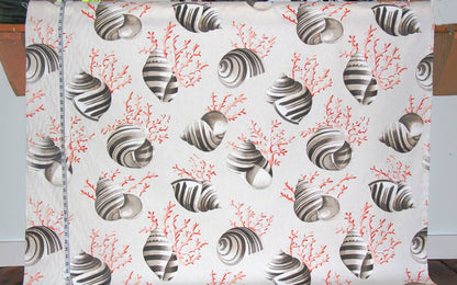 A white fabric panel featuring a repeating pattern of striped seashells and coral in gray and coral red, shown hanging flat with a measuring tape visible along the left edge.