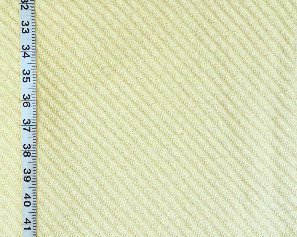 A close-up of a textured fabric with a diagonal ribbed pattern in a pale cream or light beige color, shown next to a black measuring tape ruler on the left side for scale.