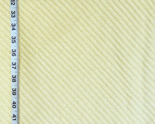 A close-up of a textured fabric with a diagonal ribbed pattern in a pale cream or light beige color, shown next to a black measuring tape ruler on the left side for scale.