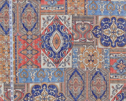 A close-up of a patterned fabric featuring a patchwork design of traditional oriental medallions and floral motifs in blue, red, beige, and orange, with a white measuring tape visible on the left side.