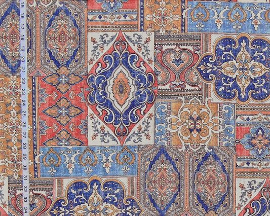 A close-up of a patterned fabric featuring a patchwork design of traditional oriental medallions and floral motifs in blue, red, beige, and orange, with a white measuring tape visible on the left side.