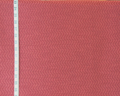 A close-up of a textured fabric with a pink and red herringbone pattern, shown next to a white measuring tape on the left side.