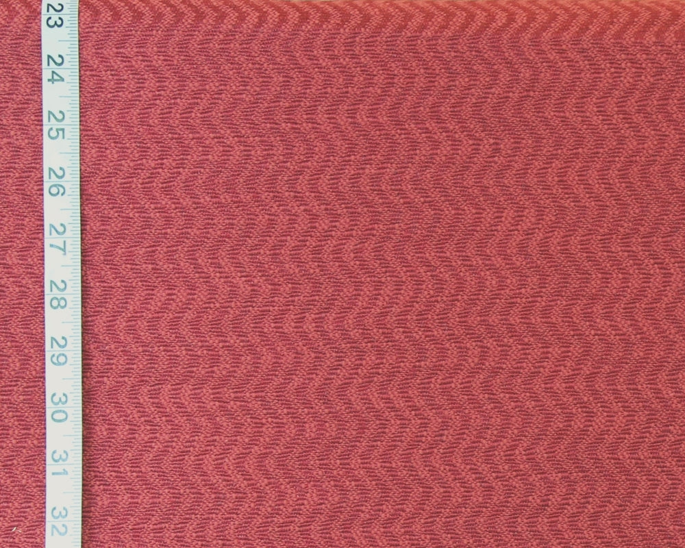 A close-up of textured fabric in a muted dusty rose or mauve pink color, shown with a white measuring tape along the left edge for scale.