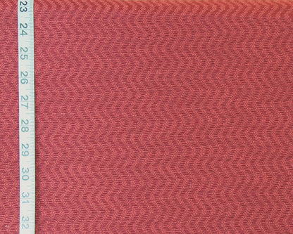 A close-up of textured fabric in a muted dusty rose or mauve pink color, shown with a white measuring tape along the left edge for scale.