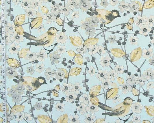 A close-up of a fabric pattern featuring small birds perched on branches with white blossoms, yellow leaves, and gray berries on a pale blue background. A ruler edge is visible along the left side for scale.
