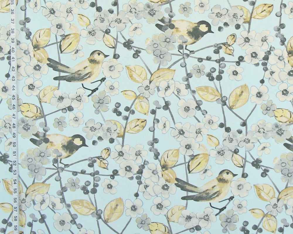 A close-up of a fabric or wallpaper pattern featuring small birds perched on branches with pale yellow leaves and white blossoms on a light blue background. A ruler edge is visible along the left side for scale.