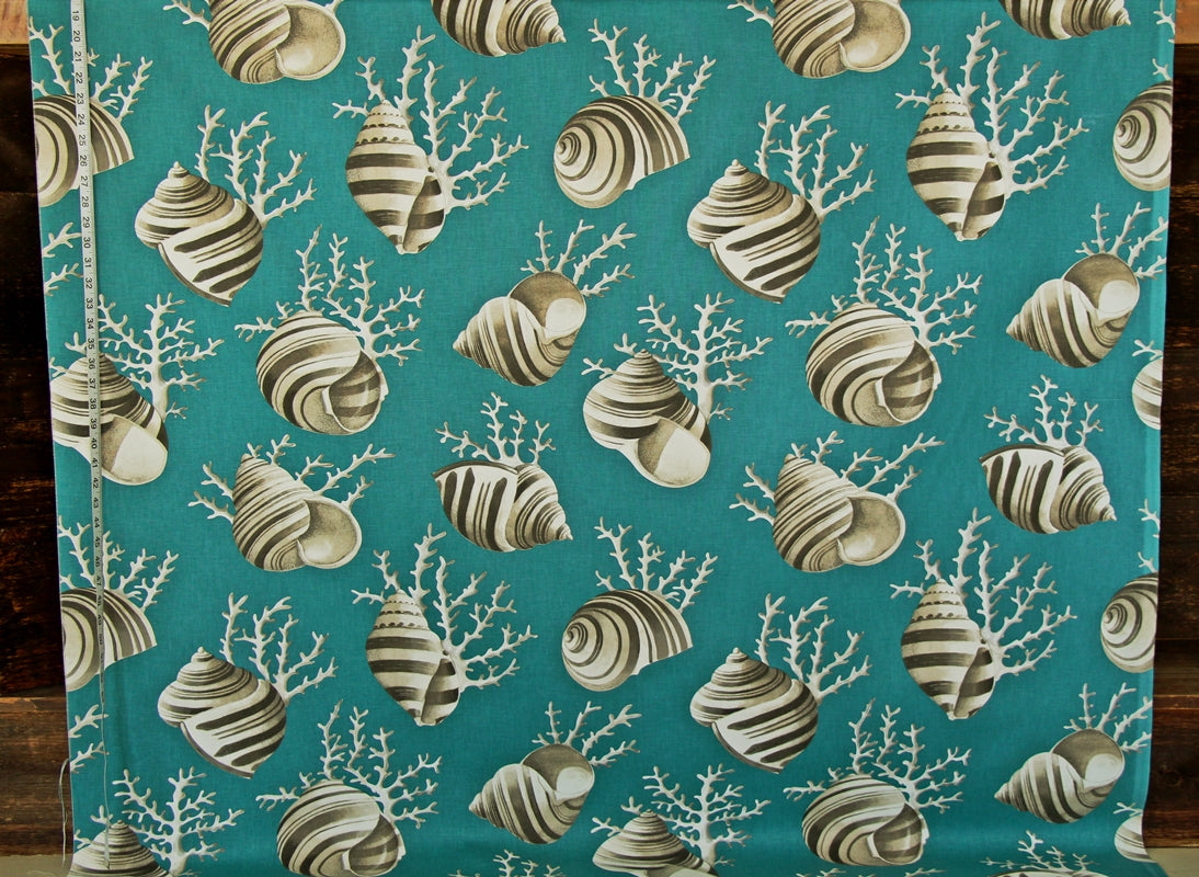 A close-up of a fabric or wallpaper pattern featuring striped seashells and white coral branches on a teal background, with a measuring tape visible along the left edge.