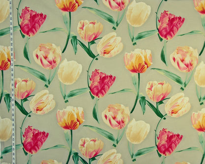 A close-up of a floral fabric or wallpaper pattern featuring tulips in pink, yellow, and orange with green leaves on a light beige background. A white measuring tape is visible along the left edge for scale.