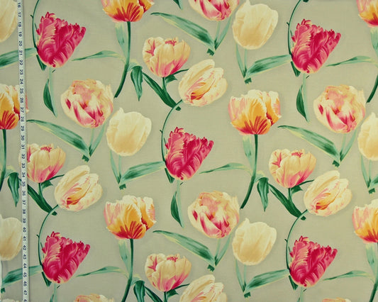 A close-up of a floral fabric or wallpaper pattern featuring tulips in pink, yellow, and orange with green leaves on a light beige background. A white measuring tape is visible along the left edge for scale.