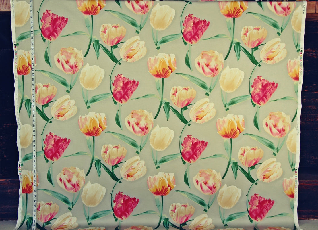 A square piece of fabric with a repeating tulip pattern on a light beige background, displayed flat with a measuring tape visible along the left edge. The tulips are in shades of yellow, pink, and orange with green stems and leaves.