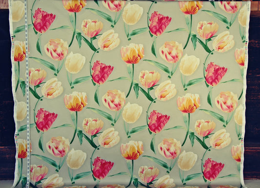 A square piece of fabric with a repeating tulip pattern on a light beige background, displayed flat with a measuring tape visible along the left edge. The tulips are in shades of yellow, pink, and orange with green stems and leaves.