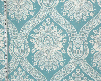 A close-up of a fabric or wallpaper pattern featuring a repeating white floral and paisley design on a turquoise blue background, with a white ruler visible along the left edge for scale.