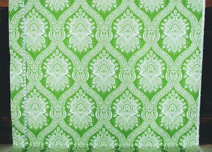 Green and white damask patterned fabric hanging flat, showing a repeating ornate floral and scroll motif.