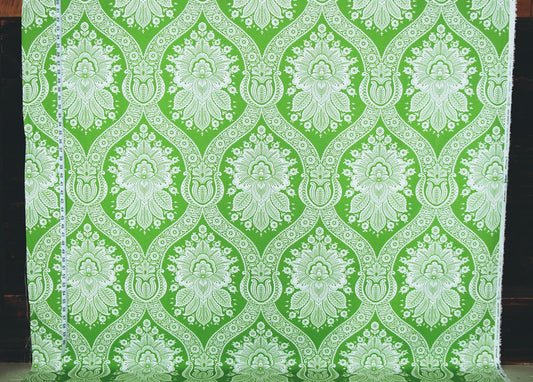 Green and white damask patterned fabric hanging flat, showing a repeating ornate floral and scroll motif.