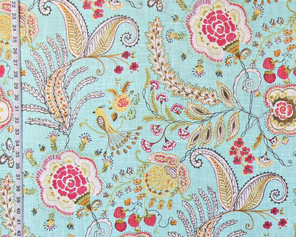 A close-up of a fabric pattern featuring a light aqua background with pink and red floral motifs, paisley details, small birds, and botanical elements. A measuring ruler is visible along the left edge to indicate scale.