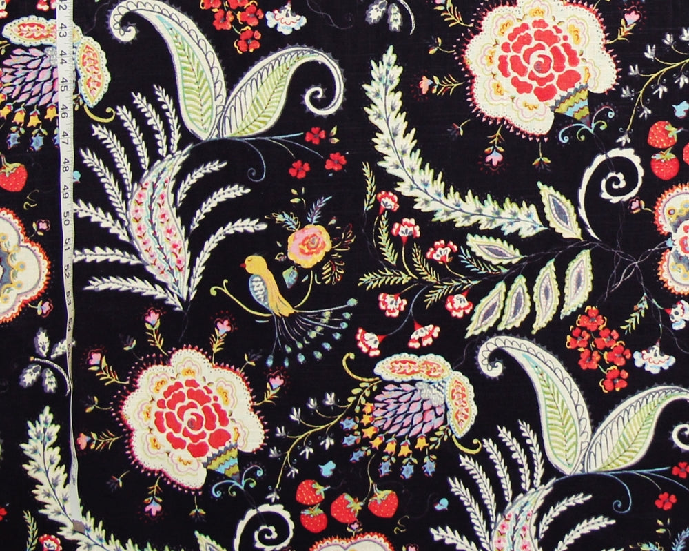 Black fabric with a colorful floral and paisley print, featuring red roses, green leaves, and yellow birds, with a white measuring tape visible on the left edge.
