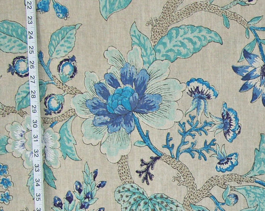 A close-up of a floral fabric print with large blue and white flowers, teal leaves, and brown branches on a light beige background, with a measuring tape visible along the left edge.