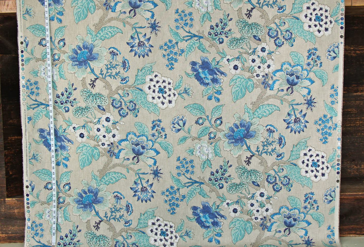 A close-up of a woven textile with an intricate floral pattern in shades of blue, teal, and white on a warm beige background, laid flat on a dark wood surface.