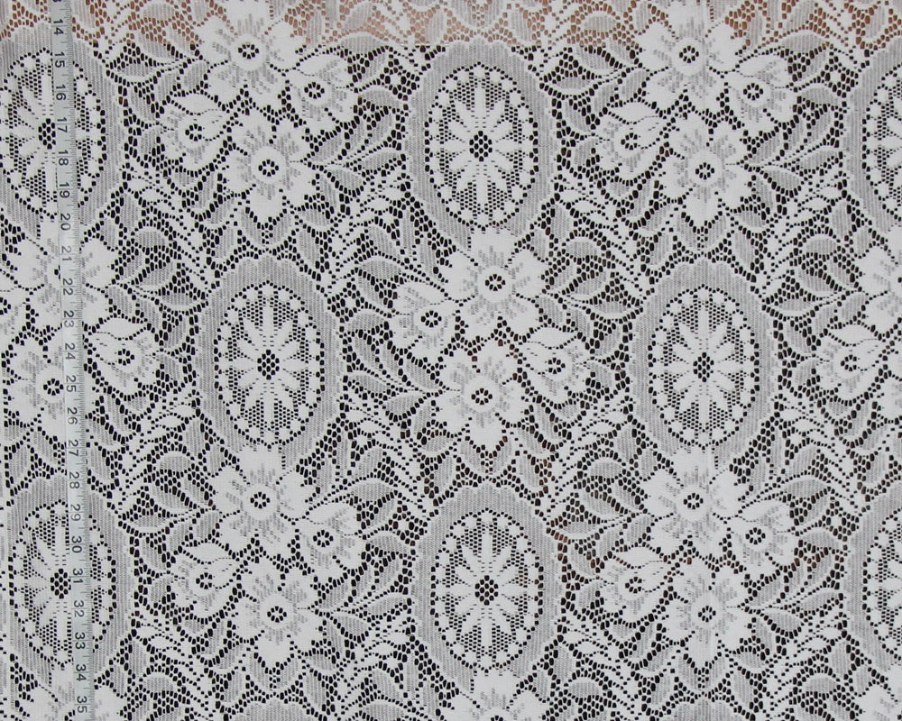 White floral lace fabric with intricate embroidered patterns and a ruler visible on the left side for scale.