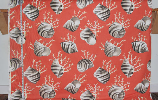 A close-up of a printed fabric with a coral and seashell pattern in orange-red, gray, and white, with a measuring tape visible along the left edge.