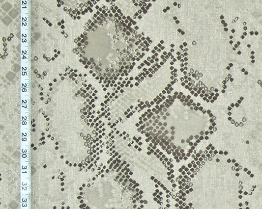 A close-up of a snakeskin-patterned fabric with a light beige base and dark brown to black dotted scales, featuring a white ruler on the left side for scale.