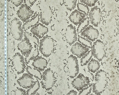 A close-up of a fabric or wallpaper pattern featuring a snakeskin design in beige, gray, and brown tones, with a white ruler visible along the left edge for scale.