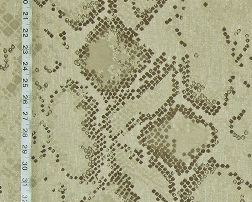 A close-up of a snakeskin-patterned fabric with a beige background and dark brown spots, featuring a white ruler on the left side for scale.