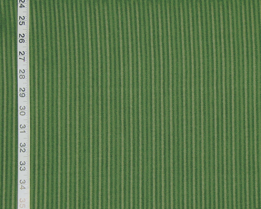A close-up of green striped fabric with alternating light and dark green vertical stripes, shown with a measuring tape along the left edge for scale.