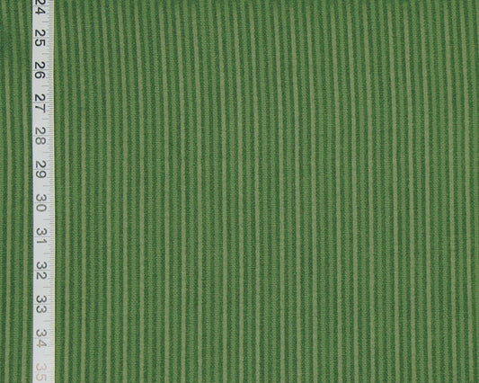 A close-up of green striped fabric with alternating light and dark green vertical stripes, shown with a measuring tape along the left edge for scale.
