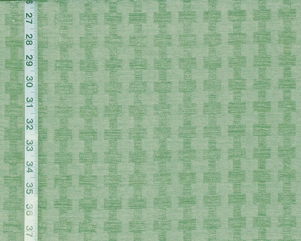 A close-up of a light green fabric with a repeating tonal geometric pattern, shown with a white measuring ruler along the left edge for scale.