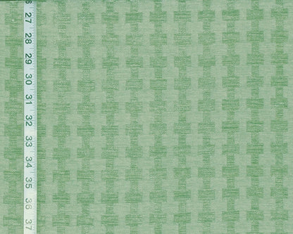 A close-up of a light green fabric with a repeating tonal geometric pattern, shown with a white measuring ruler along the left edge for scale.